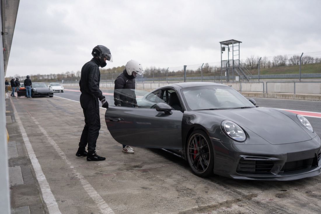 Two helmeted people prepare a car in a racetrack pit lane